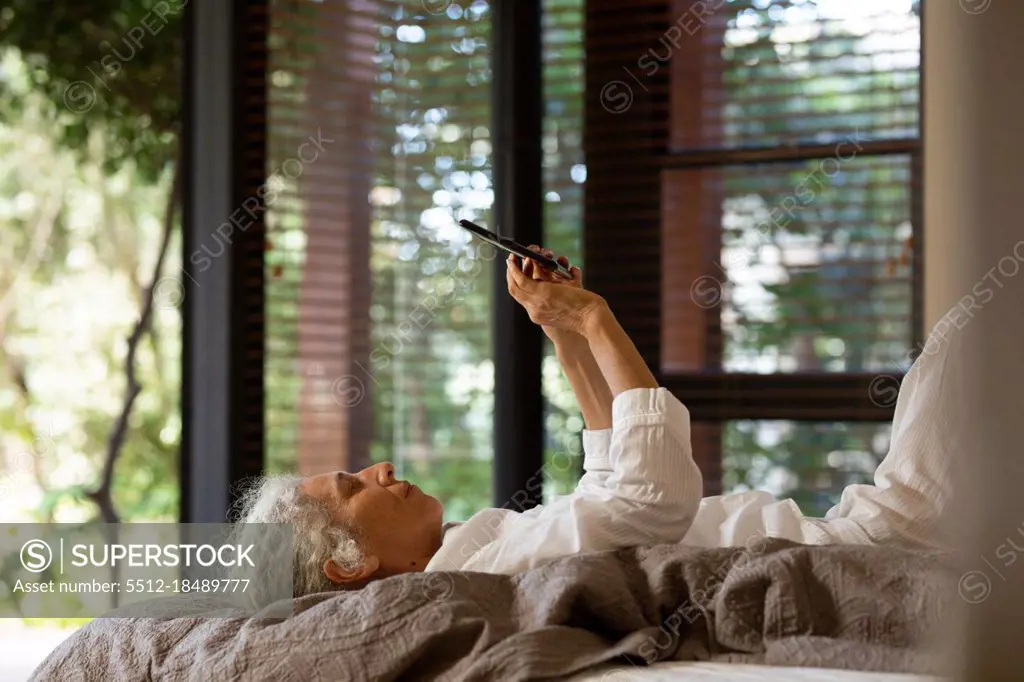 Senior caucasian woman lying on the bad and using tablet. retirement lifestyle, spending time alone at home.