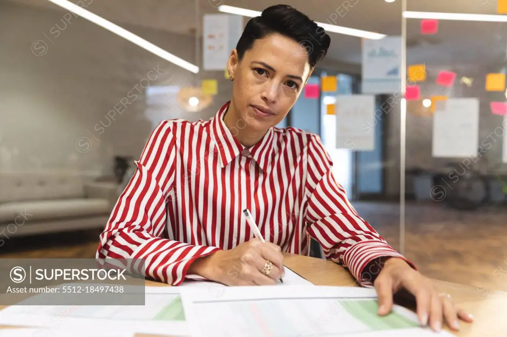 Serious caucasian female business creative sitting at desk, making notes and looking at camera. independent creative business people working at a modern office.