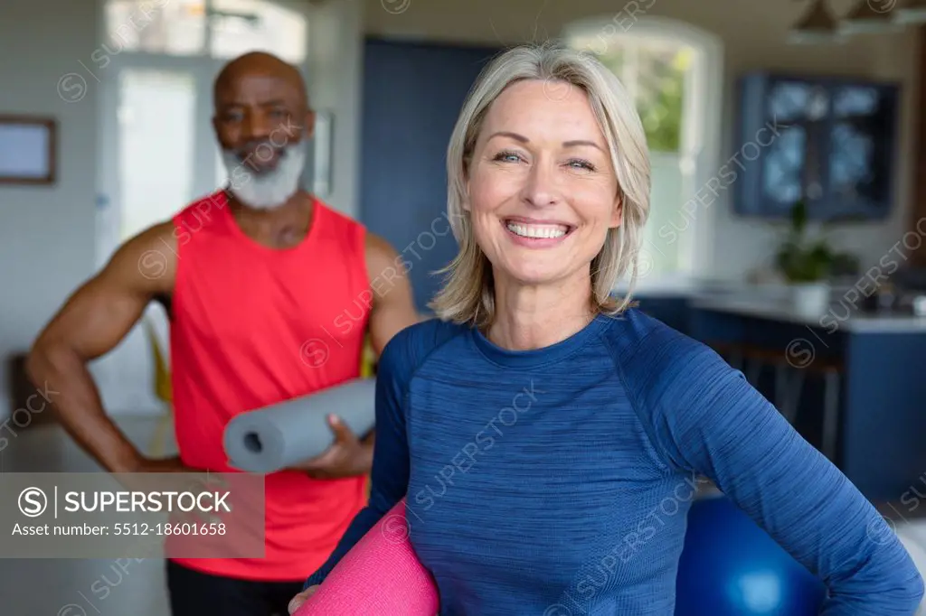 Portrait of happy senior diverse couple in exercise clothes practicing yoga, looking at camera. healthy, active retirement lifestyle at home.