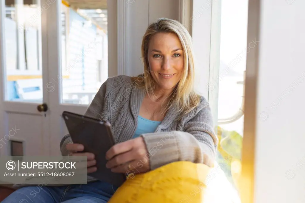 Happy caucasian mature woman using tablet in sunny living room. enjoying leisure time at home.