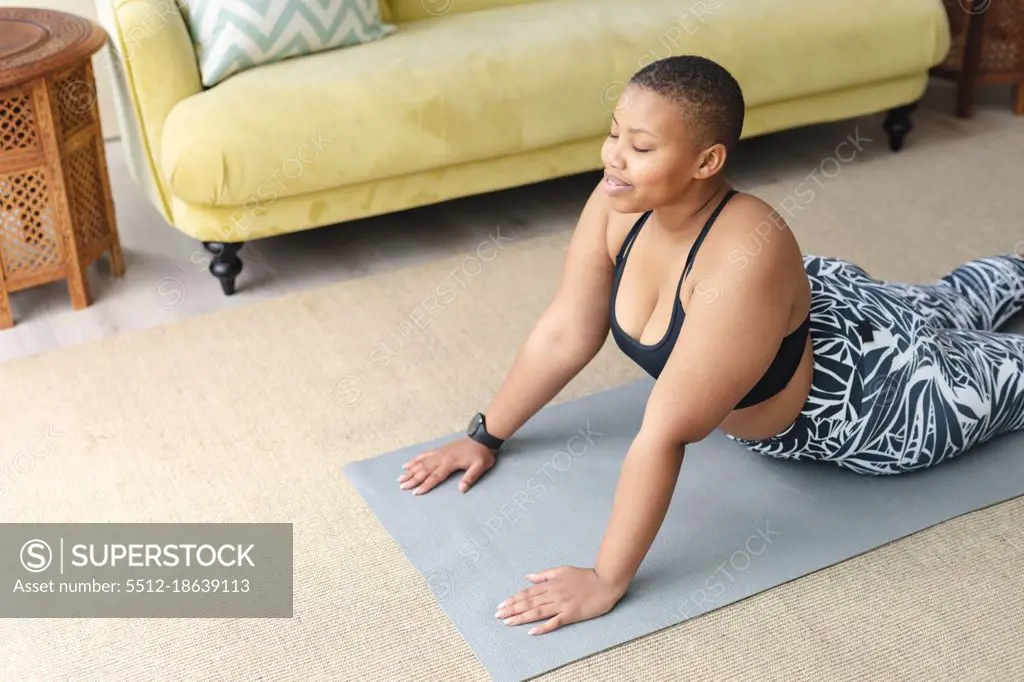 Happy african american plus size woman practicing yoga on mat at home.  fitness and healthy, active lifestyle. - SuperStock