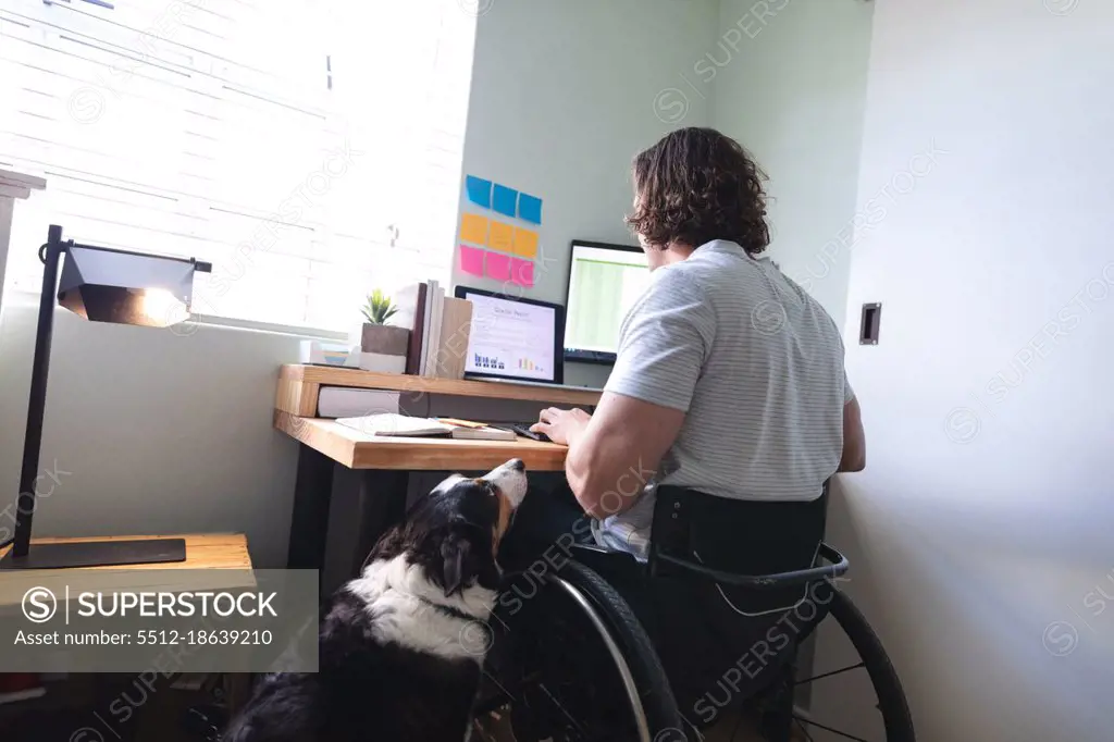 Caucasian disabled man sitting on wheelchair using laptop working from home. disability and handicap concept