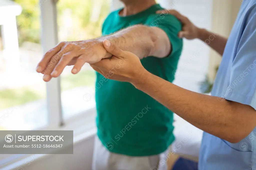 Biracial male physiotherapist treating arms of senior male patient at clinic. senior healthcare and medical physiotherapy treatment.