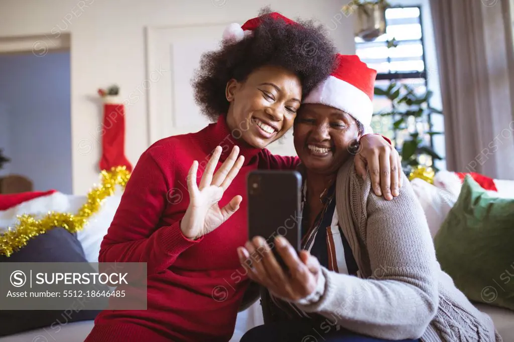 Happy african american senior woman and adult daughter in santa hats making christmas video call. christmas, festivity and communication technology.