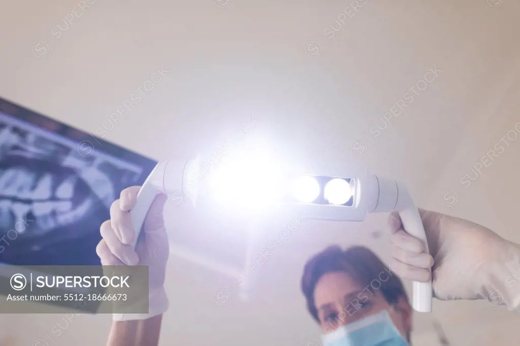 Caucasian female dental nurse wearing face mask holding lamp at modern dental clinic. healthcare and dentistry business.