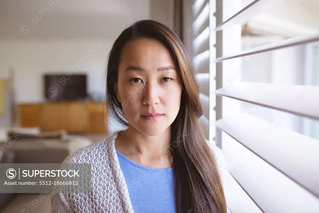 Portrait of serious asian woman standing at window, looking at camera. lifestyle, leisure and spending time at home.