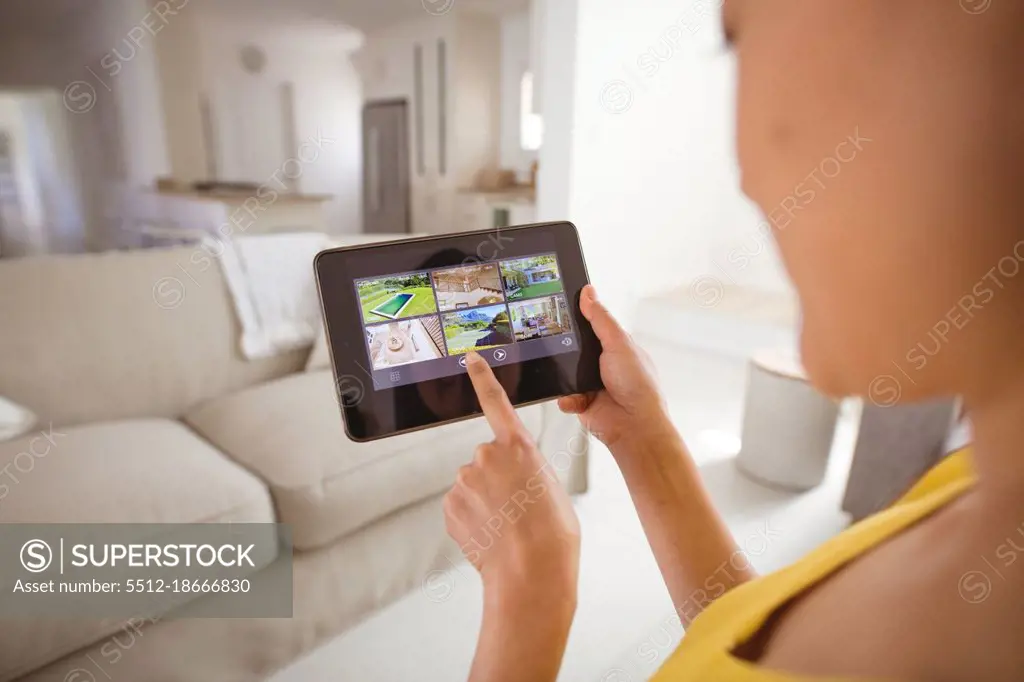 Asian woman using tablet with view from security cameras at home. security, safety, surveillance, and digital interface.