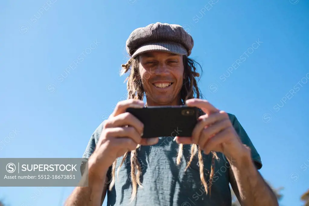 Smiling male hipster artist using smart phone against clear blue sky with copy space. technology and hipster people.