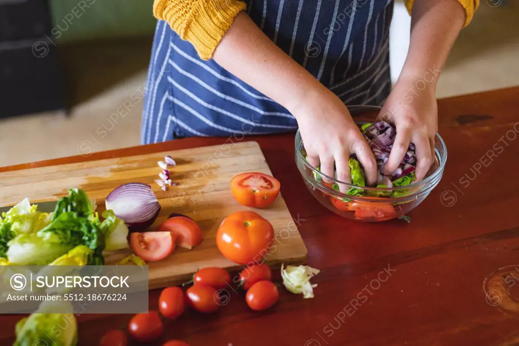 Midsection of young woman mixing freshly chopped vegetables in glass bowl at kitchen counter. domestic lifestyle and healthy eating.