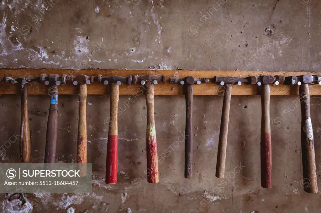 Various hammers hanging side by side on hook rack mounted on wall in industry. forging, metalwork and manufacturing industry.