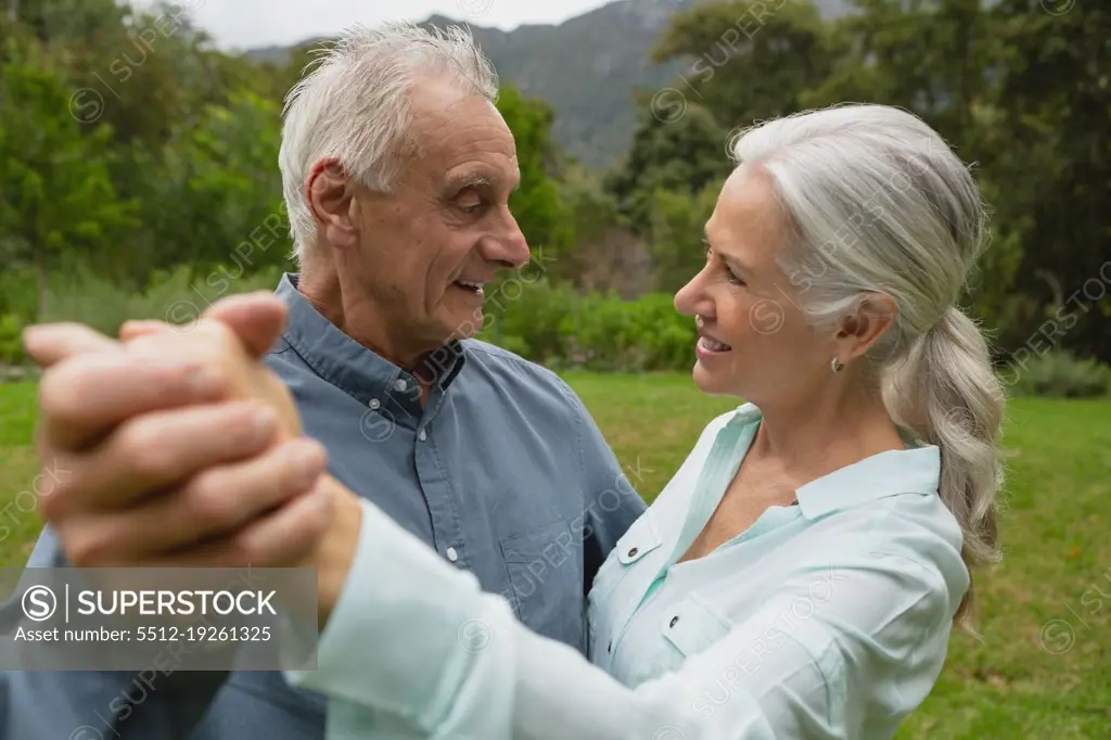 Side view of happy active Caucasian senior couple dancing together in the garden