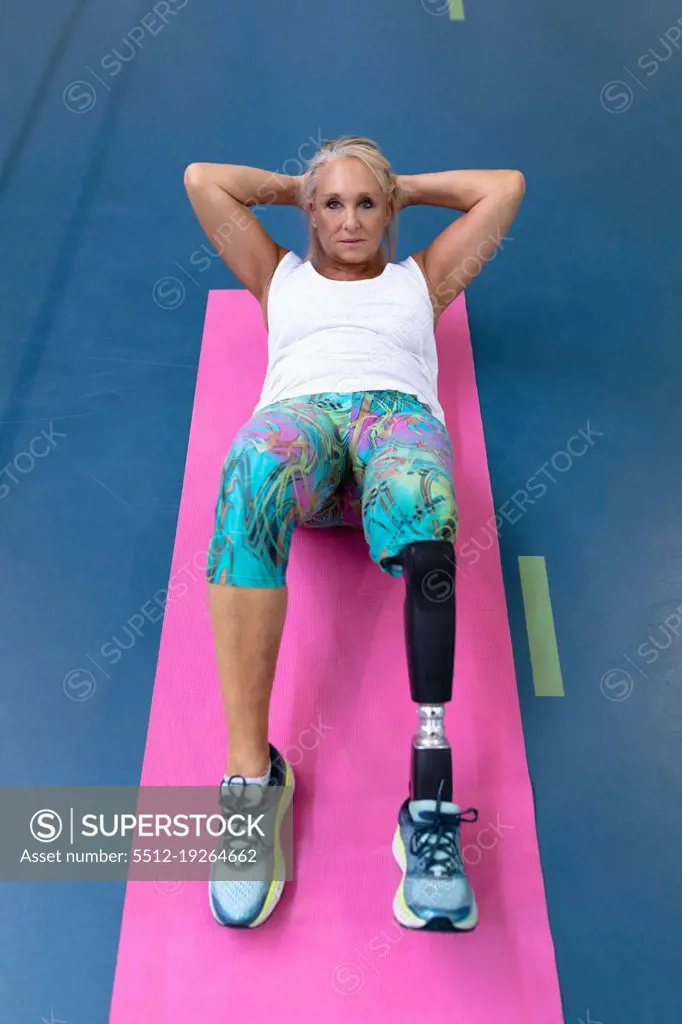 High angle view of Caucasian disabled active senior woman exercising on exercising mat in sports center. Sports Rehab Centre with physiotherapists and patients working together towards healing