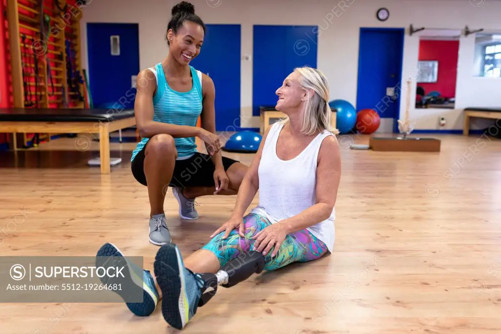 Front view of African-american female trainer talking with disabled Caucasian active senior woman in sports center. Sports Rehab Centre with physiotherapists and patients working together towards healing