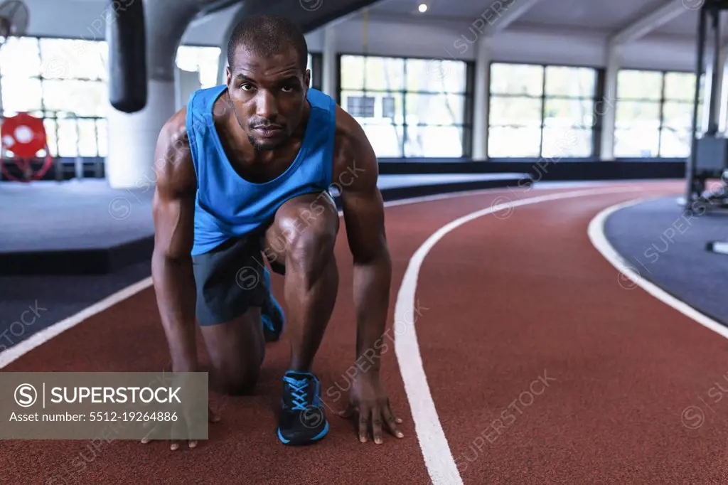 Portrait of African-american male athletic in starting position on running  track in fitness center. Bright modern gym with fit healthy people working  out and training - SuperStock