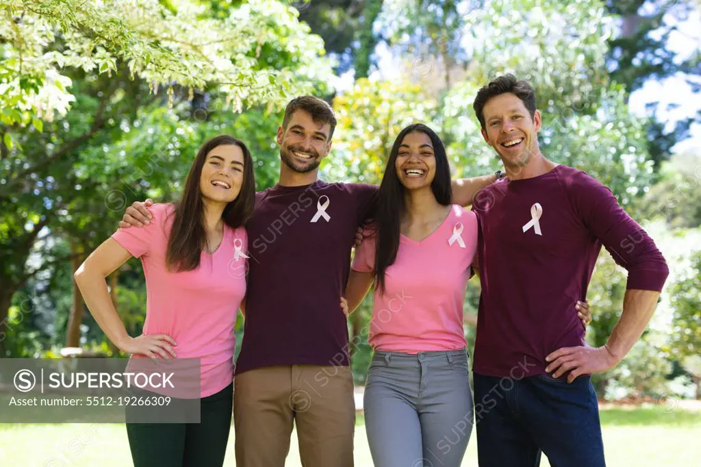 Portrait of smiling multiracial men and women wearing breast cancer awareness ribbons in park. breast cancer awareness campaign, friendship and unity concept.