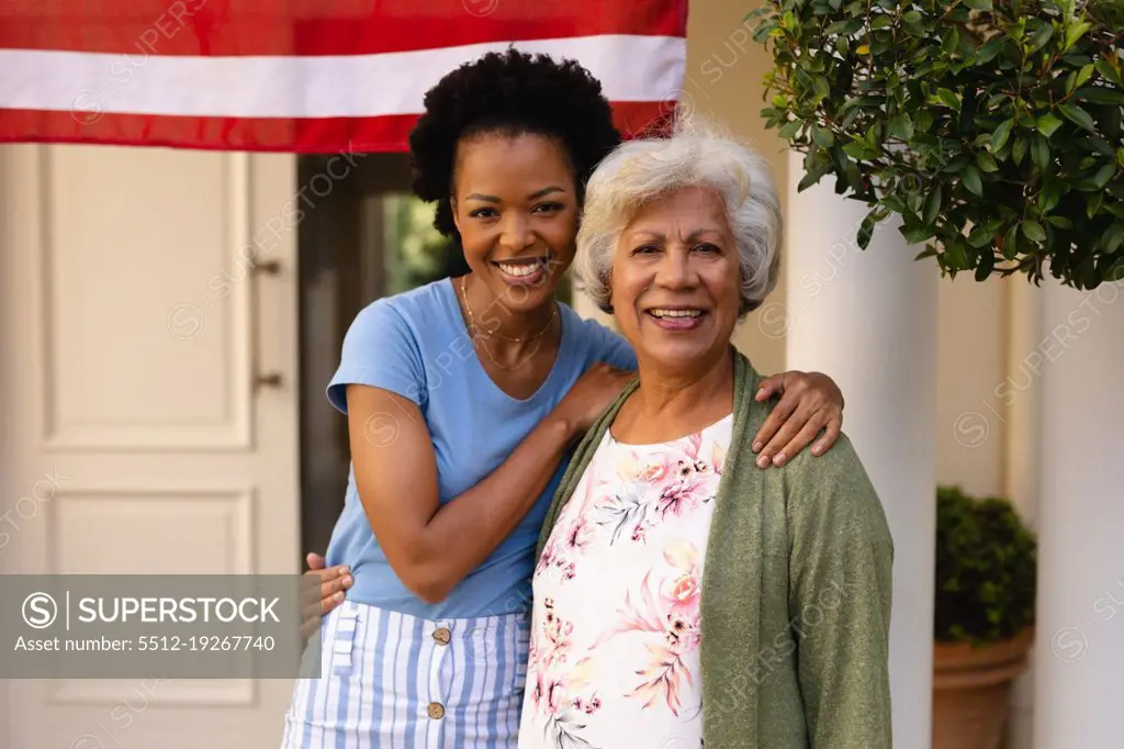 Portrait of smiling african american daughter with arm around mother at house entrance. family and bonding, unaltered