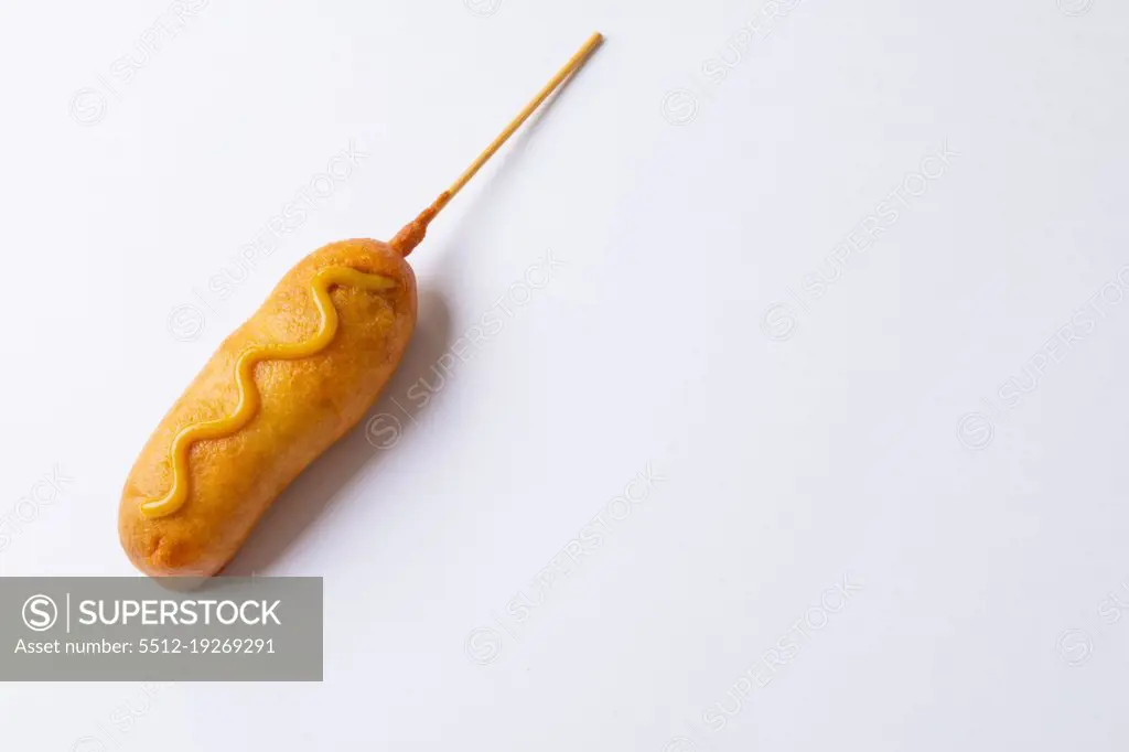 Close-up of corn dog with mustered sauce over skewer on white background with copy space. unaltered, copy space, unhealthy food, meat, sausage and fried food.