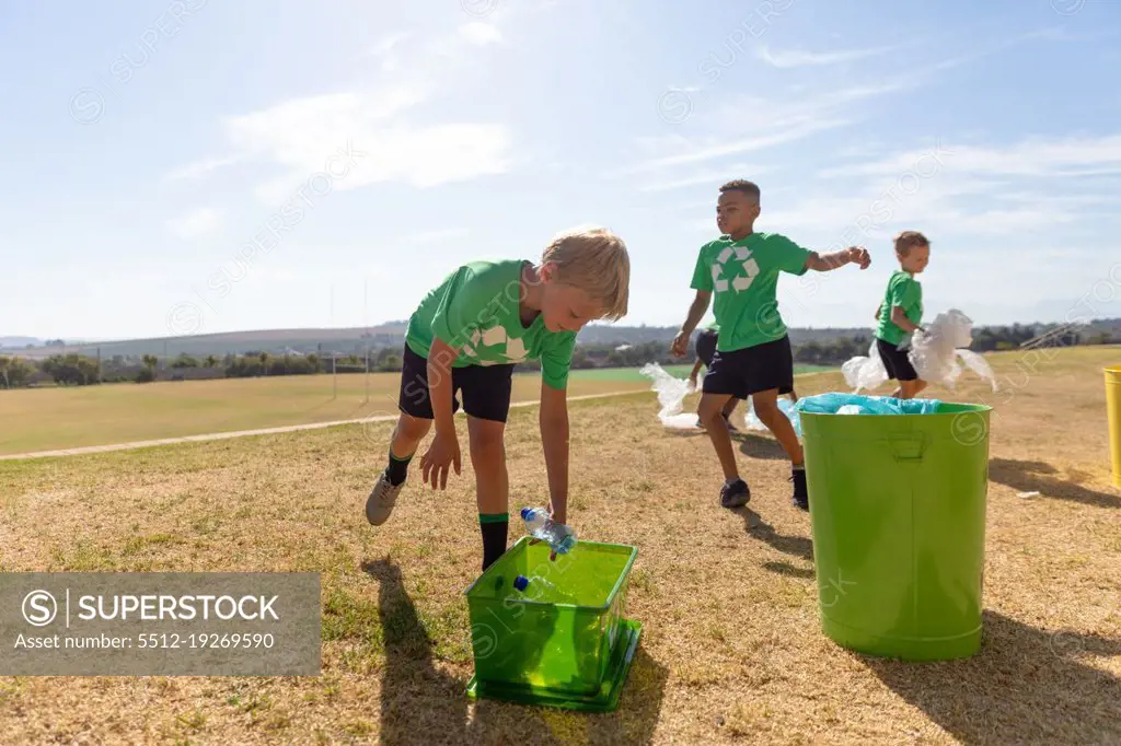 Multiracial elementary schoolboys putting plastic garbage in garbage bin on school ground. unaltered, sustainable lifestyle, teamwork, cleaning, responsibility and recycling concept.