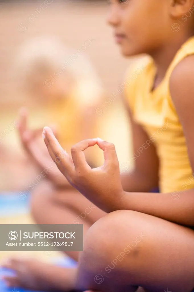 Biracial elementary schoolgirl meditating while sitting on ground. unaltered, childhood, education, activity, sports training, yoga and physical education concept.