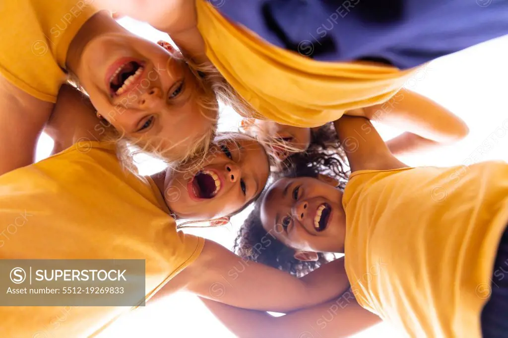 Directly below portrait of cheerful multiracial elementary schoolgirls huddling while standing. unaltered, childhood, education, teamwork, together, sports training and sports activity concept.