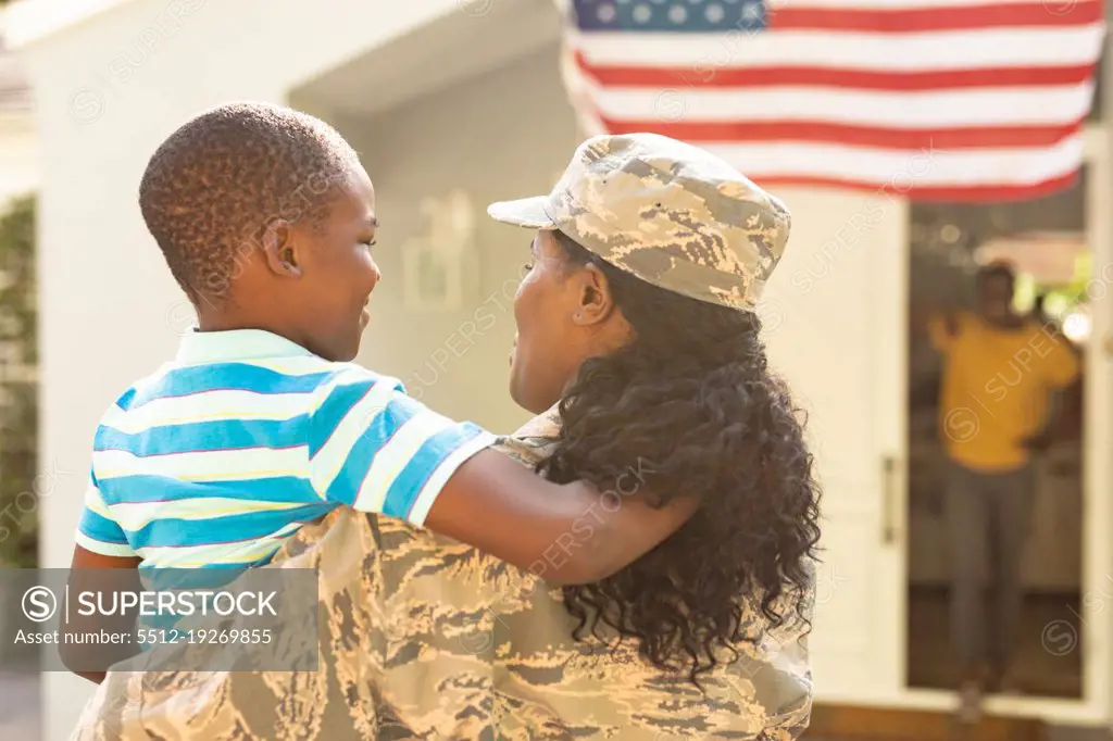 Happy female mid adult african american soldier carrying son on arrival at home. unaltered, pride, military, arrival, homecoming, armed forces and patriotism concept.