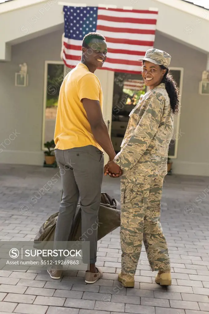 Portrait of smiling female mid adult african american soldier holding hand of husband on arrival. unaltered, pride, homecoming, american flag, military, arrival, armed forces and patriotism.