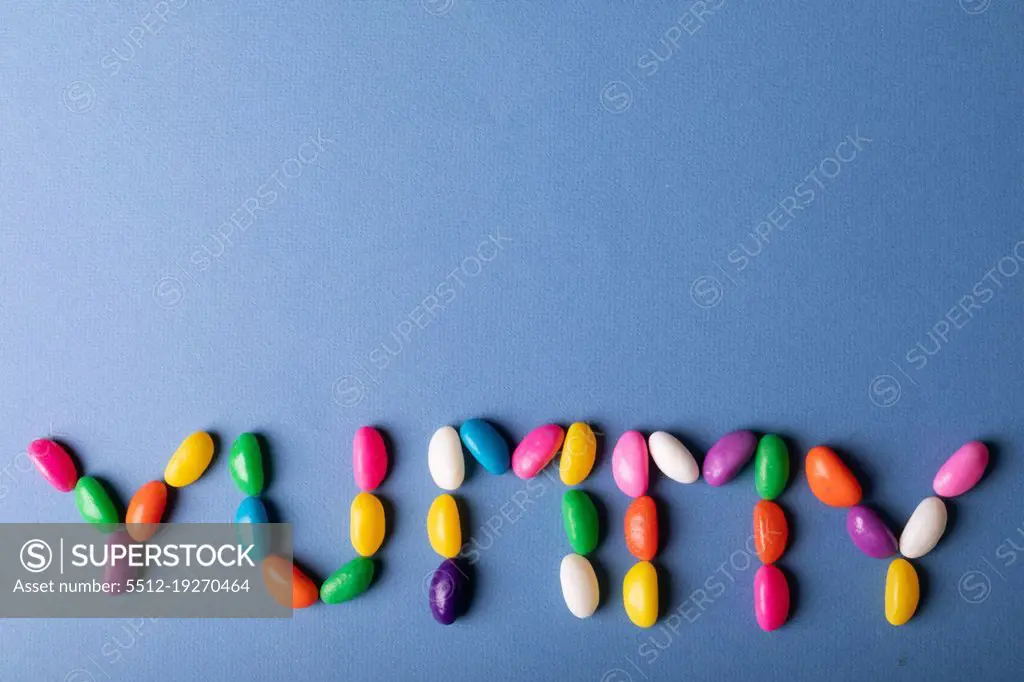 Directly above view of colorful candies arranged as yummy word on blue background with copy space. unaltered, sweet food and unhealthy eating concept.