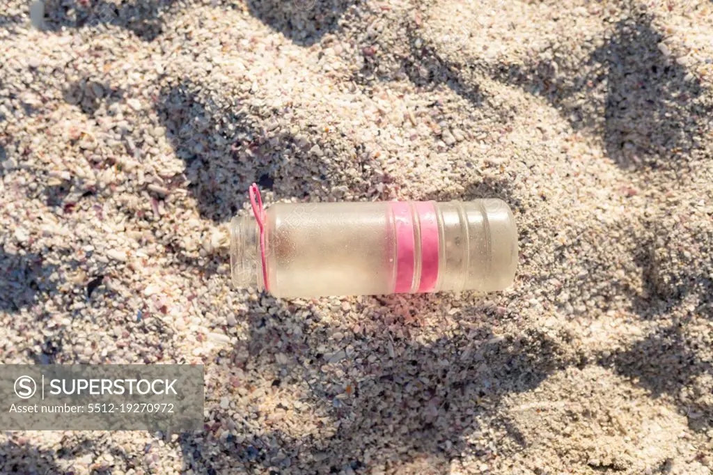 Directly above view of abandoned plastic bottle on white sand at beach during sunny day. unaltered, environmental damage and plastic pollution concept.