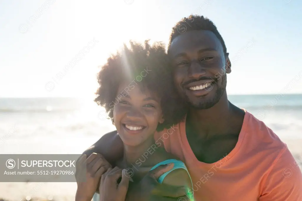 Back lit portrait of smiling african american couple enjoying summer holiday at beach on sunny day. unaltered, lifestyle, love, togetherness and holiday concept.