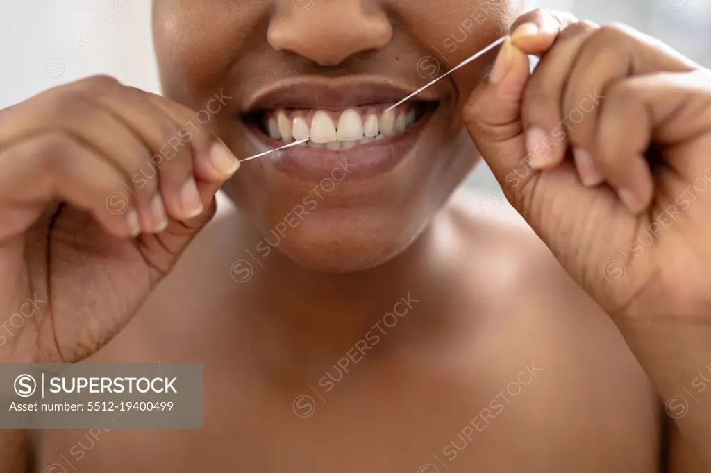 Close-up of african american mid adult woman using dental floss in bathroom. unaltered, dental health, lifestyle, hygiene, routine.