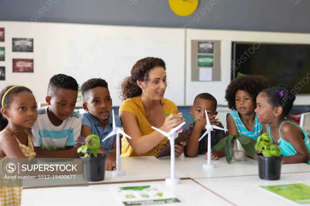 African american elementary students listening to caucasian young female teacher showing windmill. unaltered, education, environment, teaching, sustainable lifestyle and school concept.