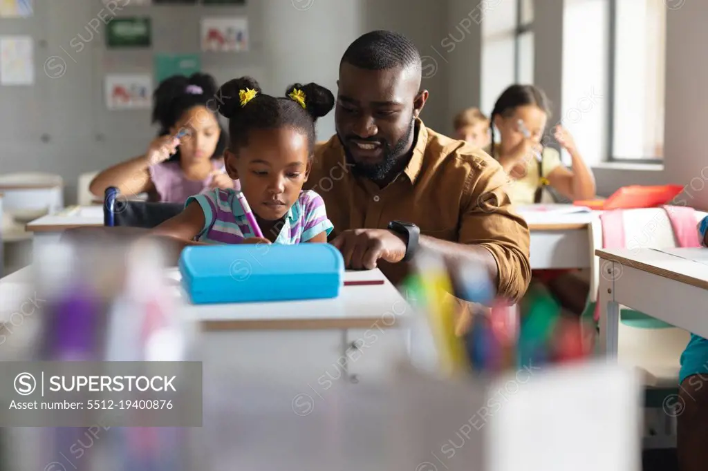 African american young male teacher teaching african american elementary girl on wheelchair in class. unaltered, education, childhood, teaching, learning, physical disability and school concept.