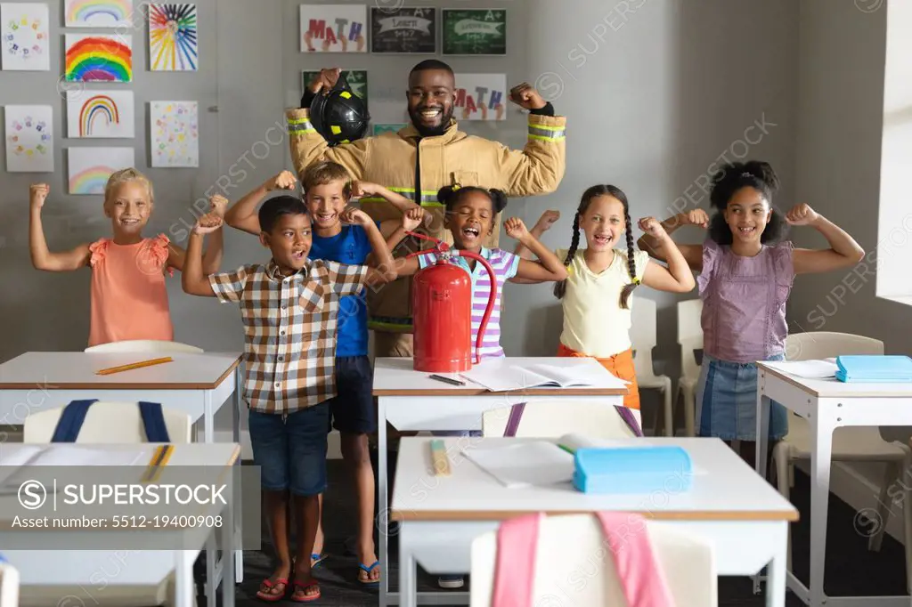 Multiracial elementary students and african american young male teacher flexing muscles. unaltered, education, firefighter, safety, protection, teaching and school concept.