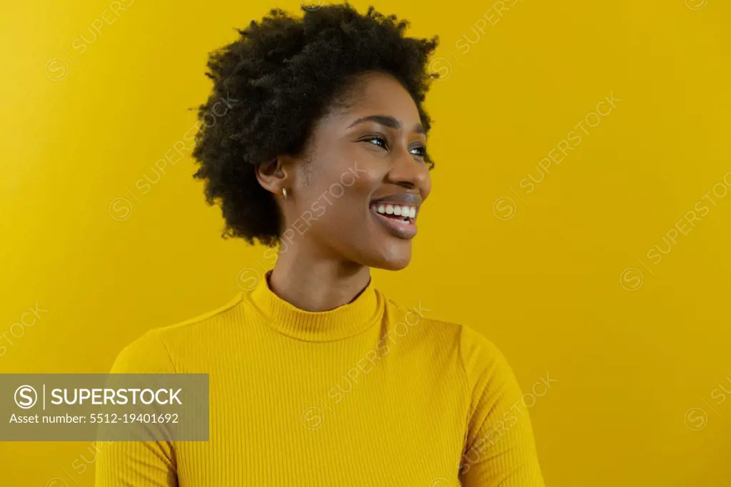 Cheerful young african american businesswoman with afro hairstyle looking away against yellow wall. unaltered, business, people and emotions concept.