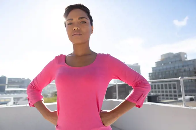 Serious looking woman standing confident for breast cancer awareness in pink shirt against urban background