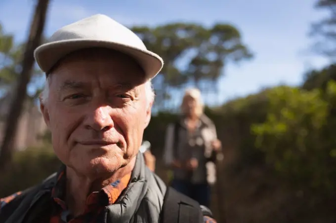 Portrait close up of a mature Caucasian man smiling to camera, with a Caucasian woman and countryside behind him