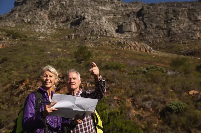 Front view close up of a mature Caucasian man and woman reading a map and pointing during a walk in a rural setting, with mountains in the background