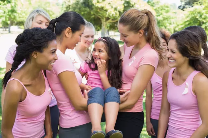 Happy female volunteers carrying girl during breast cancer campaign at park