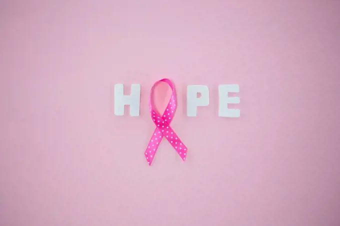 Overhead view of spotted Breast Cancer Awareness ribbon with HOPE text on pink background