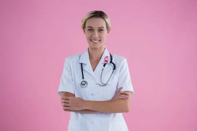 Portrait of confident female doctor with arms crossed standing against pink background