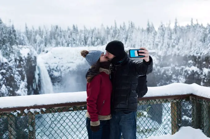 Couple taking selfie with mobile phone near waterfall during winter
