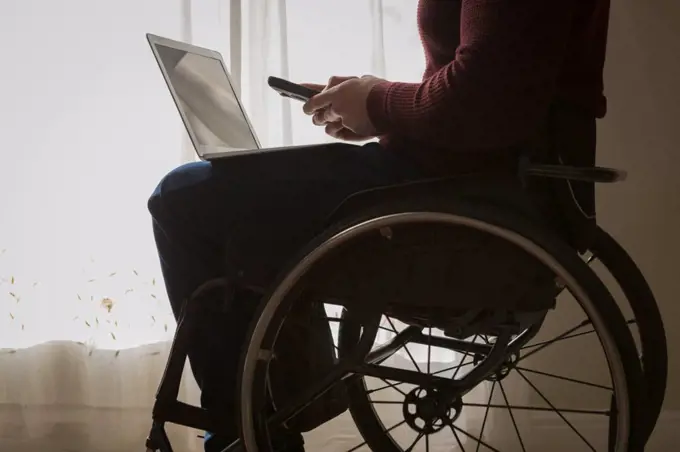 Mid section of disabled man using mobile phone at home