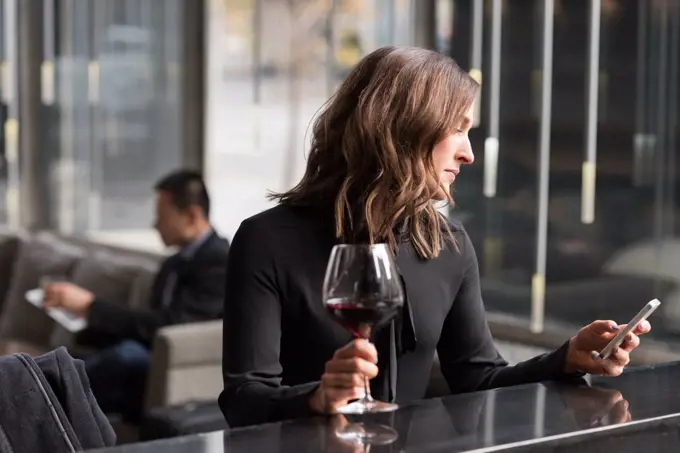 Businesswoman having red wine while using mobile phone in hotel