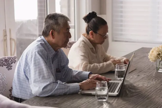 Senior couple using laptop and digital tablet on dining table at home