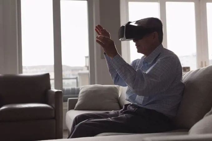 Senior man using virtual reality headset on sofa in living room at home
