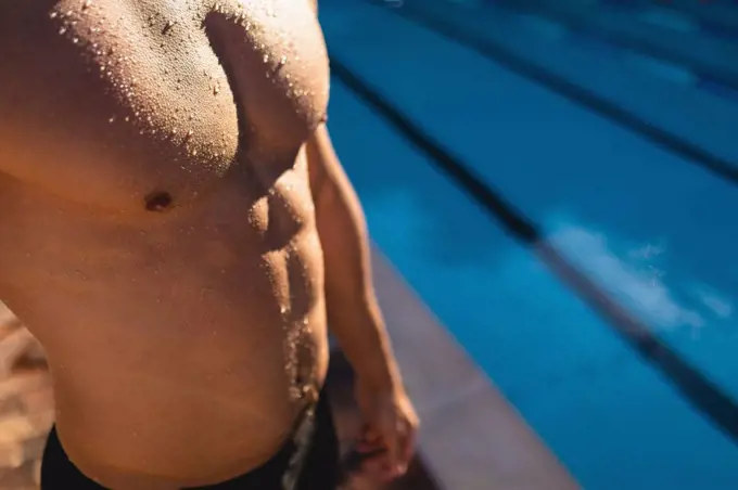 Mid section of a male Caucasian swimmer standing near the swimming pool on a sunny day