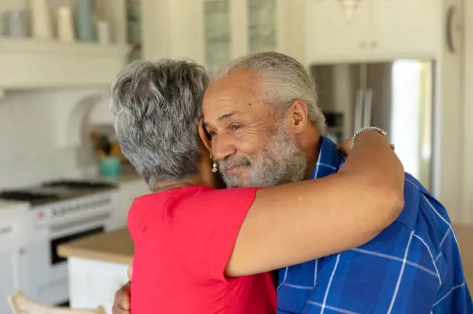 Self isolation in quarantine lock down. side view close up of a senior mixed race couple at home in their luxury kitchen, embracing and smiling