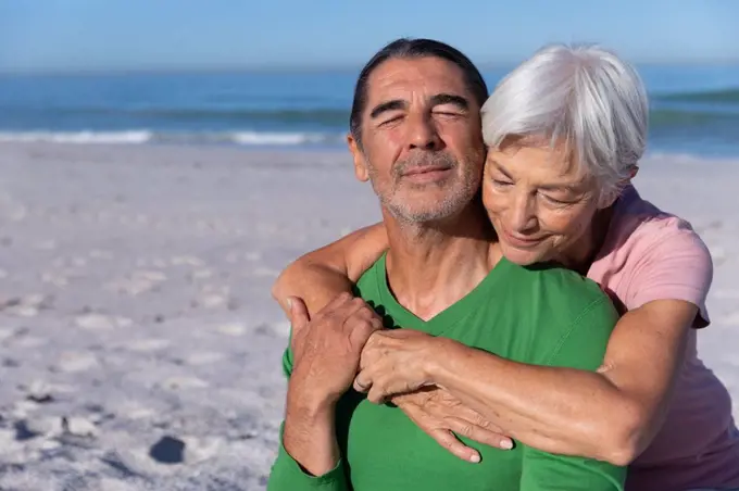 Senior Caucasian couple enjoying time at the beach, a woman is embracing a man from behind