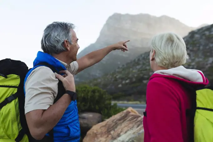 Senior couple spending time in nature together, walking in the mountains, man is pointing on the mountains. healthy lifestyle retirement activity.