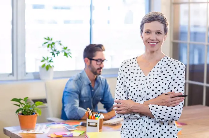 Smiling woman standing arms crossed with her partner behind in the office